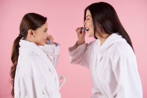 Mother and daughter in gowns brushes teeth.